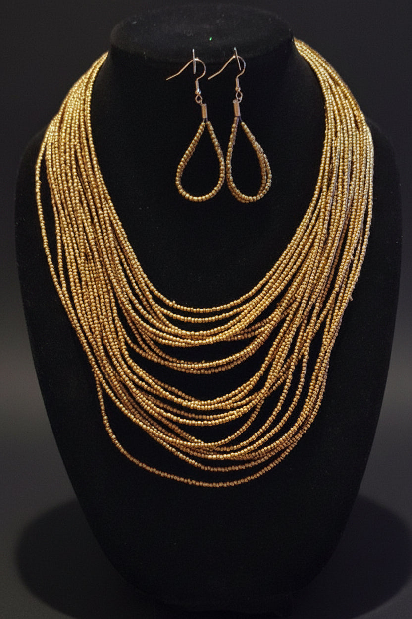 A gold beaded multi-strand statement necklace displayed on a black mannequin bust, accompanied by matching gold teardrop dangle earrings.