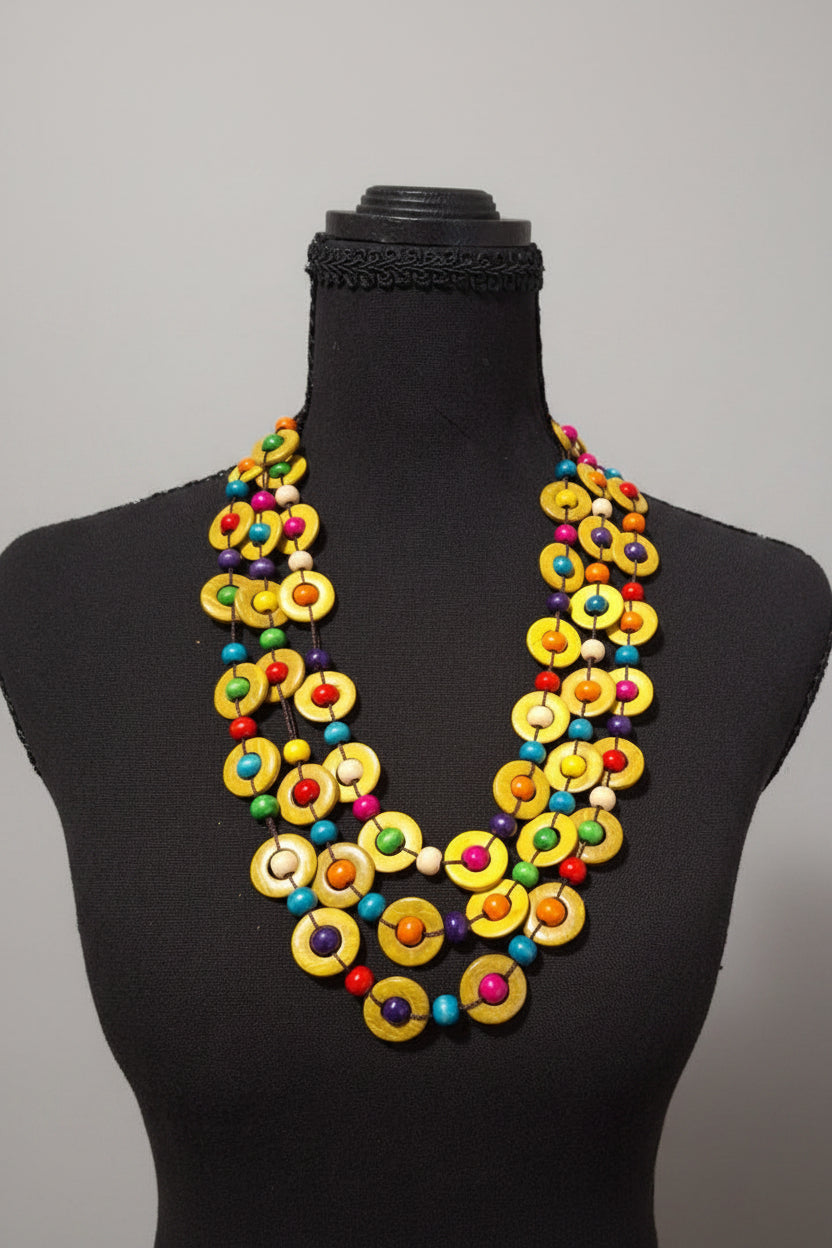 A colorful beaded necklace displayed on a black mannequin bust against a black background. The necklace features multiple strands of yellow circular beads with small multicolored accents.