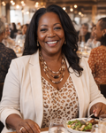 Woman sitting at a dining table with a plate of food, smiling.