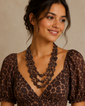 A woman wearing a dark brown floral lace top with puff sleeves and a multi-strand dark brown floral beaded necklace, set against a neutral beige background.