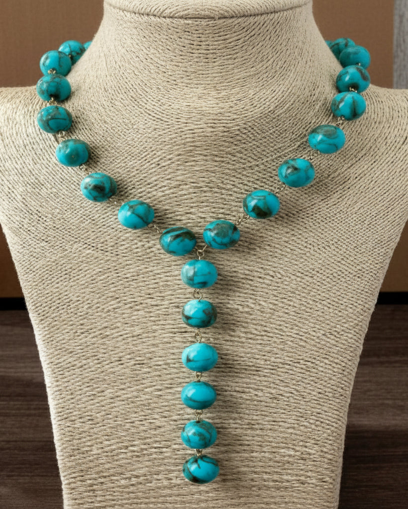 A turquoise bead necklace displayed on a beige fabric jewelry bust against a brown background.