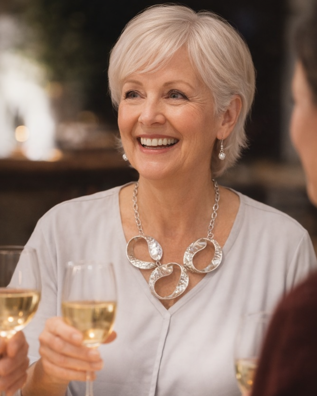 Woman enjoying a meal with a glass of wine, smiling at the camera.