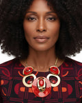 Woman wearing a patterned top and large, colorful necklace on a white background