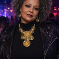 Woman wearing a large gold necklace and earrings with a dark background