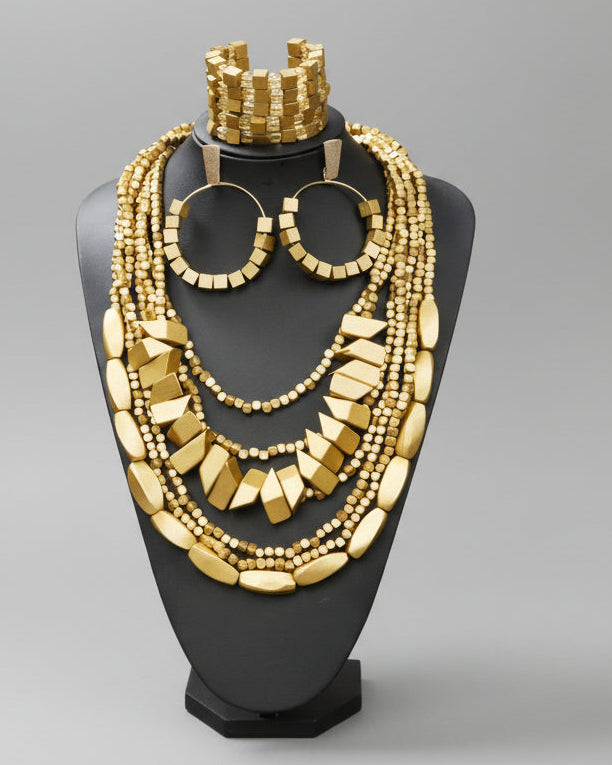 Gold jewelry set including necklace, earrings, and bracelet on a black stand against a brown background.
