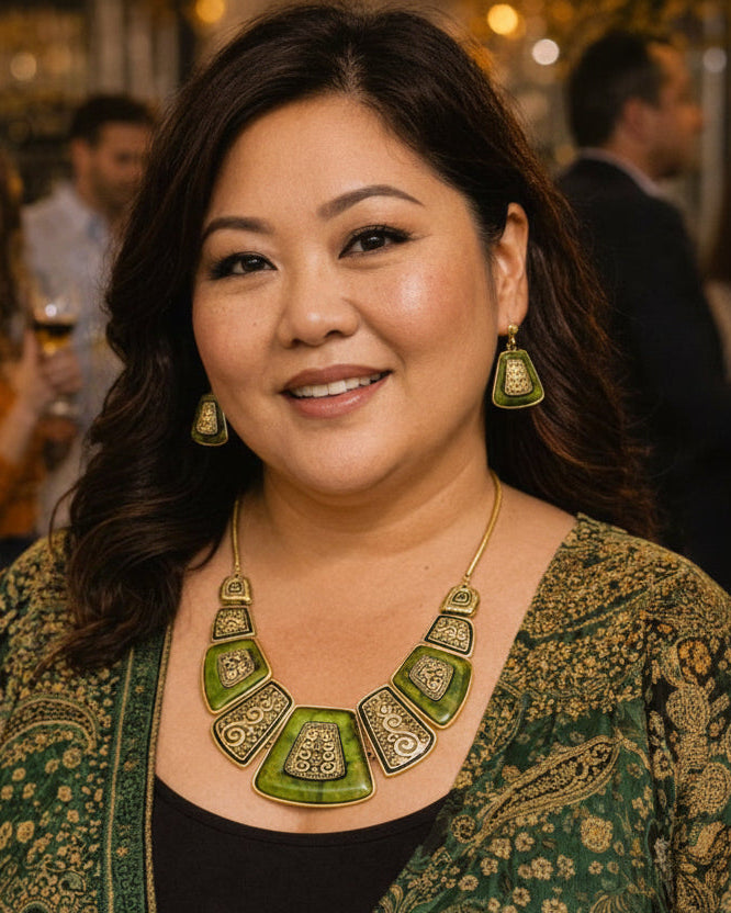Woman wearing a green and gold necklace with a patterned garment in a social setting
